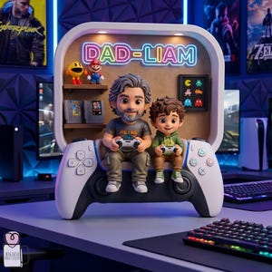May include: A decorative gaming-themed figurine featuring a father and son seated on a large white and black game controller. The figurine has a neon sign that reads "DAD-LIAM". The background includes video game posters and consoles.