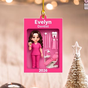 May include: A rectangular pink ornament featuring the name Evelyn and the title Dentist. It displays a cartoon character in pink scrubs holding a coffee cup, alongside dental tools, a tooth with braces, toothpaste, and a dental chair, with 2026.