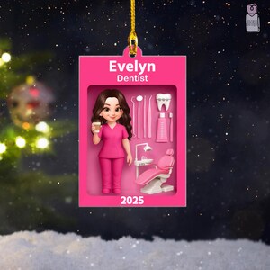 May include: A rectangular pink hanging ornament featuring the name Evelyn and the title Dentist. It displays a cartoon character in pink scrubs holding a cup, alongside dental tools, a tooth with braces, toothpaste, and a dental chair, dated 2025.