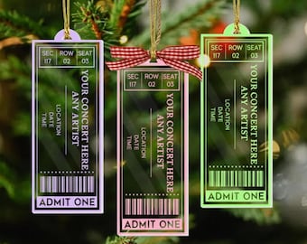 May include: Three transparent concert ticket ornaments in purple, pink, and green, hanging from gold cords. Each features the text "YOUR CONCERT HERE" and "ADMIT ONE." The tickets have a section, row, and seat number.