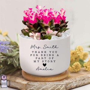 May include: White ceramic planter with a pink succulent plant. The planter has the text "Mrs. Smith Thank You For Being A Part Of My Story Amelia" printed on it.
