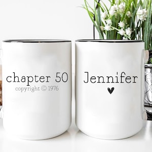 May include: Two white ceramic mugs with black handles and rims. One mug reads "chapter 50 copyright © 1976" and the other mug reads "Jennifer" with a heart symbol. The mugs are part of a gift set.