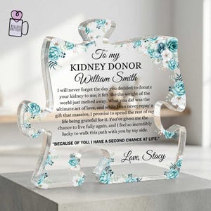 May include: A clear acrylic puzzle piece plaque featuring teal and white floral accents. The text reads: To my KIDNEY DONOR William Smith, followed by a message of gratitude and the closing: BECAUSE OF YOU, I HAVE A SECOND CHANCE AT LIFE. Love, Stacy.