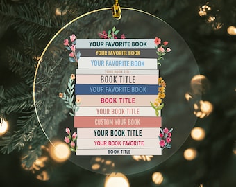 May include: A round, clear glass ornament with a stack of colorful books. The books have the text "YOUR FAVORITE BOOK" repeated multiple times, with the words "BOOK TITLE" in between. The ornament is decorated with floral accents.
