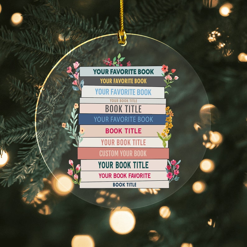 May include: A round, clear glass ornament with a stack of colorful books. The books have the text "YOUR FAVORITE BOOK" repeated multiple times, with the words "BOOK TITLE" in between. The ornament is decorated with floral accents.