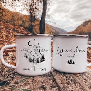 May include: Two white enamel mugs with black designs. One mug has a mountain range with a crescent moon and stars. The other mug has the text "Logan & Jenia 4.28.12".