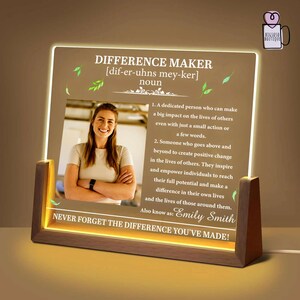 May include: A wooden-framed LED light with the text "DIFFERENCE MAKER" and a definition. Includes a photo of a woman and the text "NEVER FORGET THE DIFFERENCE YOU'VE MADE!"