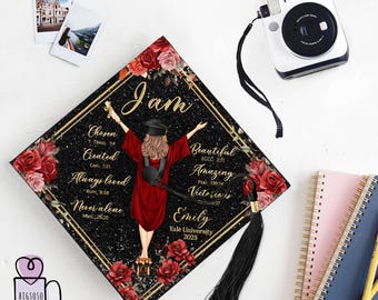 May include: A black graduation cap with a gold trim and a black tassel. The cap is decorated with red roses and a silhouette of a woman in a red graduation gown. The text "I am" is written in gold letters on the cap, along with several Bible verses. The text "Emily, Yale University, 2025" is also written on the cap.