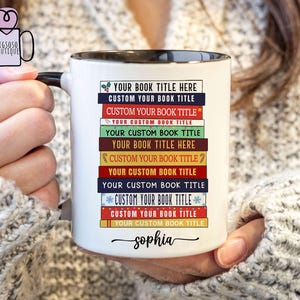 May include: White ceramic mug with a black rim and handle. The mug has a design of stacked books with the text "YOUR BOOK TITLE HERE" repeated multiple times. The name "sophia" is written at the bottom of the mug.