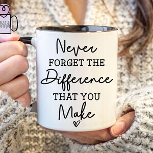 May include: White ceramic mug with a black rim and handle. The mug has black text that reads "Never forget the difference that you make" with a small heart symbol at the bottom.