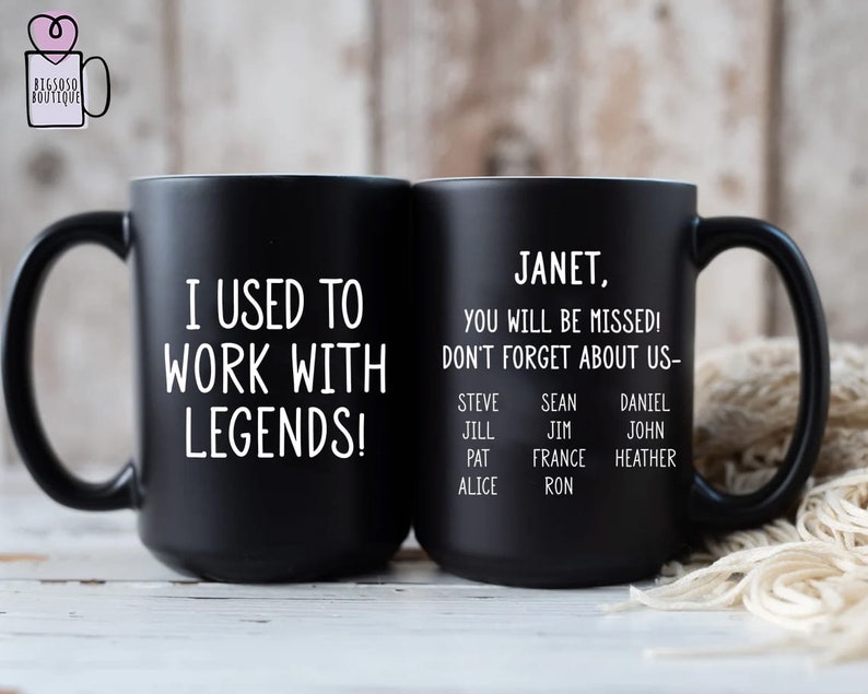 K&ouml;nnte beinhalten: Zwei schwarze Keramikbecher. Auf einem Becher steht in wei&szlig;er Schrift "I USED TO WORK WITH LEGENDS!". Der andere Becher tr&auml;gt die Aufschrift "JANET, YOU WILL BE MISSED! DON'T FORGET ABOUT US-" mit einer Namensliste. Die Becher haben schwarze Griffe.
