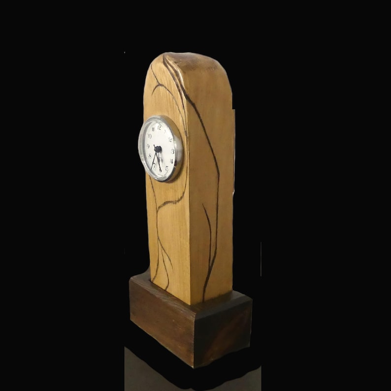 Puede incluir: Un reloj de madera con acabado marr&oacute;n claro y base marr&oacute;n oscuro. La esfera del reloj es redonda con marco plateado y manecillas negras. L&iacute;neas marrones oscuras decoran los lados del reloj.