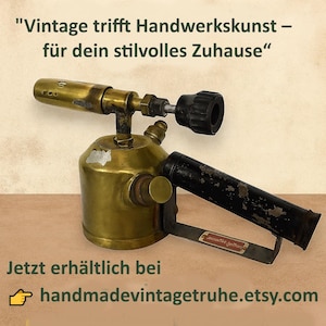 Op de afbeelding: Een vintage messing brander met een zwarte handgreep en mondstuk. De brander heeft een cilindrische brandstoftank en een lange, schuine mondstuk. De tekst "Vintage trifft Handwerkskunst - für dein stilvolles Zuhause" staat bovenaan. De tekst "handmadevintagetruhe.etsy.com" staat onderaan.