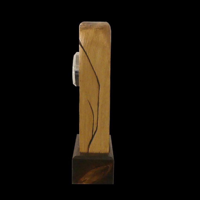 Puede incluir: Un reloj de escritorio de madera con forma rectangular. El reloj tiene un acabado marr&oacute;n claro con una base marr&oacute;n oscuro. Una esfera de reloj plateada es visible en el lateral. Un dise&ntilde;o de l&iacute;neas negras est&aacute; en la parte delantera.
