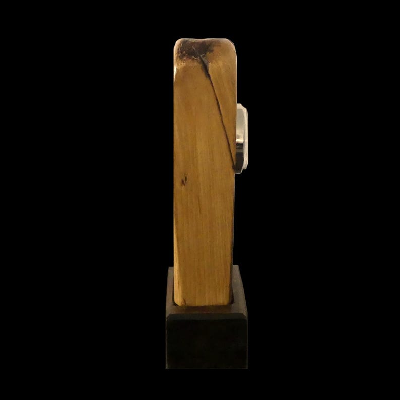 Puede incluir: Un reloj de madera con un acabado natural, con una esfera plateada. El reloj es rectangular y se apoya sobre una base oscura y cuadrada. La veta de la madera es visible, lo que a&ntilde;ade encanto r&uacute;stico.
