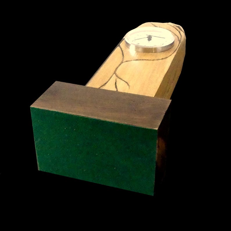 Puede incluir: Un reloj de escritorio de madera con un cuerpo de madera de color claro y una base marr&oacute;n oscuro. La esfera del reloj es redonda con un borde plateado. La base est&aacute; cubierta de fieltro verde. L&iacute;neas negras decorativas est&aacute;n grabadas en la madera.