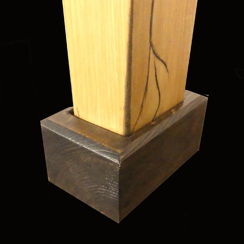 Puede incluir: Una escultura de madera con una secci&oacute;n superior rectangular de color claro, con un dise&ntilde;o lineal oscuro, colocada sobre una base rectangular marr&oacute;n oscuro. El contraste de la madera clara y oscura crea un efecto visual llamativo. Es una obra de arte moderna.