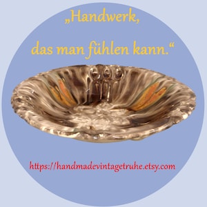 Könnte beinhalten: Eine ovale Keramikschale mit strukturierter, gewellter Oberfläche. Die Schale hat eine Mischung aus Braun-, Grau- und Orangetönen. Der Text "Handwerk, das man fühlen kann." ist gelb, und die Etsy-Shop-URL ist rot.
