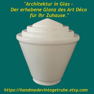 Può includere: Un paralume in vetro bianco con una parte superiore a gradini e un corpo conico largo. Il testo in alto recita: "Architektur in Glas - Der erhabene Glanz des Art Déco für Ihr Zuhause." Il testo in basso recita: "https://handmadevintageruhe.etsy.com".