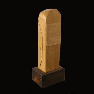 Puede incluir: Escultura de madera hecha a mano con base rectangular y parte superior redondeada. El cuerpo principal es de color marr&oacute;n claro con un peque&ntilde;o cuadrado de color m&aacute;s claro adjunto. Una l&iacute;nea oscura y curva recorre el lateral.
