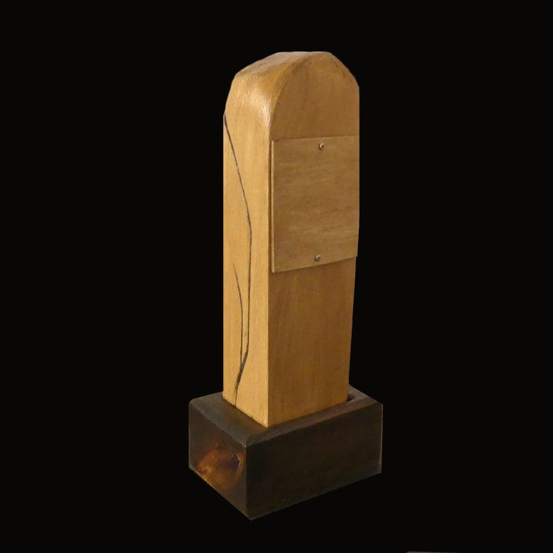 Puede incluir: Escultura de madera hecha a mano con base rectangular y parte superior redondeada. El cuerpo principal es de color marr&oacute;n claro con un peque&ntilde;o cuadrado de color m&aacute;s claro adjunto. Una l&iacute;nea oscura y curva recorre el lateral.