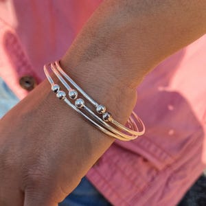 Puede incluir: Tres pulseras de plata con pequeñas cuentas redondas en la muñeca de una persona.