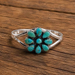 May include: A silver cuff bracelet featuring a central flower-shaped cluster of nine teardrop-shaped turquoise stones. The metal band splits into two arms on each side, connecting to the floral centrepiece which has a dark oxidised finish.