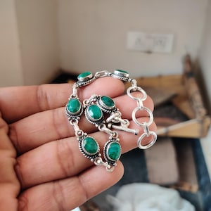 Pode incluir: Uma pulseira de prata com pedras preciosas ovais verdes vibrantes. A pulseira tem um design decorativo em torno de cada pedra e um fecho de alternância. As pedras preciosas são definidas em uma configuração de metal prateado.