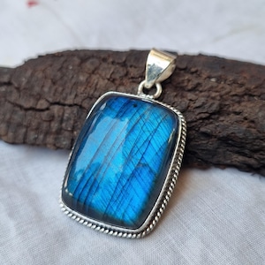 Könnte beinhalten: Ein silberner Anhänger mit einem großen, rechteckigen blauen Labradorit-Edelstein. Der Edelstein hat einen schimmernden, irisierenden Effekt.