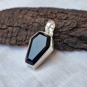 May include: A silver pendant shaped like a coffin with a black gemstone in the center.