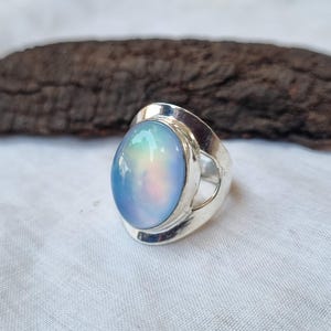 May include: A silver ring featuring a large oval iridescent blue gemstone. The ring has a distinctive open design on the band.