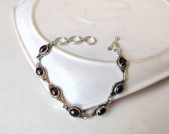 May include: A silver bracelet with a toggle clasp and oval-shaped garnet stones.
