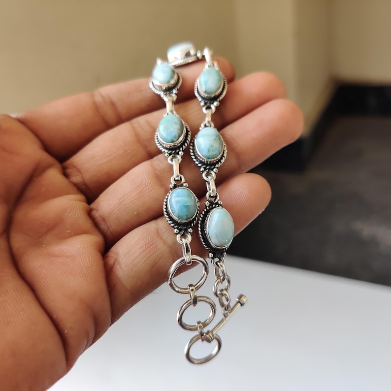 May include: A silver bracelet featuring oval-shaped, light blue gemstones. The bracelet has a toggle clasp and is composed of multiple gemstone links. The gemstones are set in a decorative silver setting.
