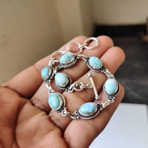 Può includere: Un bracciale in argento con pietre preziose ovali azzurro chiaro. Il bracciale ha una chiusura a levetta ed è composto da più maglie di pietre preziose. Le pietre sono incastonate in una cornice d'argento decorativa.