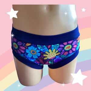 Könnte beinhalten: Dunkelblaue Unterwäsche mit einem lebendigen Blumenmuster in Blau-, Gelb-, Rosa- und Lilatönen. Die Unterwäsche hat einen einfarbigen dunkelblauen Bund und Besatz. Das Blumenmuster zeigt stilisierte Blumen und Blätter.