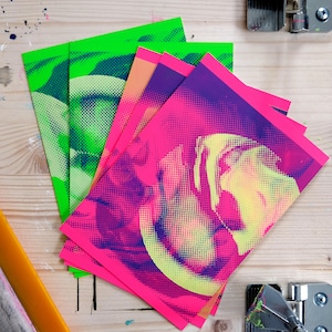 Può includere: Un mazzo di quattro fogli di carta stampati. Il foglio superiore è rosa con un design astratto viola e giallo. Gli altri fogli sono verdi con un design astratto blu e bianco.