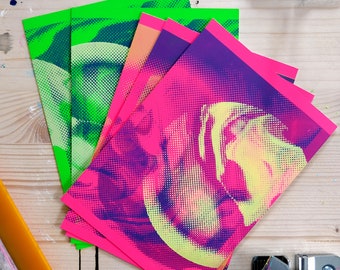 May include: A stack of four printed sheets of paper. The top sheet is pink with a purple and yellow abstract design. The other sheets are green with a blue and white abstract design.