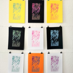 May include: Nine abstract art prints featuring a wavy pattern in various colour combinations. The prints are displayed on a white wall using clips.