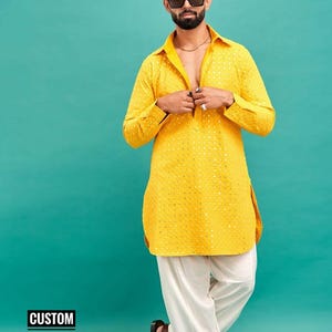 May include: A yellow kurta with a white embroidered pattern. The kurta has a collar and long sleeves. The model is wearing white trousers and brown sandals. The text "CUSTOM KURTAS" is visible in the bottom left corner of the image.
