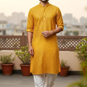 Puede incluir: Kurta amarillo mostaza con un pequeño estampado floral, combinado con pantalones blancos. El kurta tiene cuello mandarín y cierre de botones. También se ve el texto "CUSTOM KURTAS".
