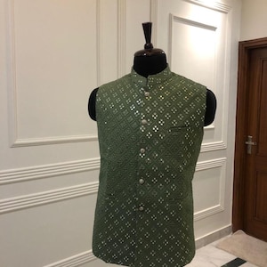 Op de afbeelding: Olijfgroen geborduurd vest met een opstaande kraag en zilverkleurige knopen. Het vest heeft een geometrisch patroon en wordt op een mannequin getoond. De tekst "COUSTOM KURTAS" is zichtbaar.