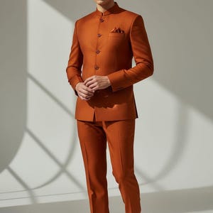 May include: A rust-colored suit with a mandarin collar, pocket square, and matching trousers. The suit is worn with brown dress shoes. The text "CUSTOM KURTAS" is visible at the bottom of the image.