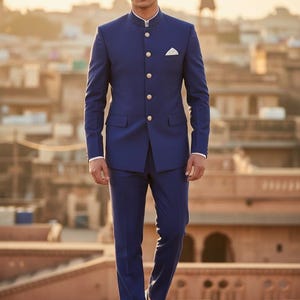 May include: A navy blue suit with a mandarin collar and gold buttons. The suit includes a matching jacket and pants. A white pocket square is visible. The text "CUSTOM KURTAS" is at the bottom of the image.