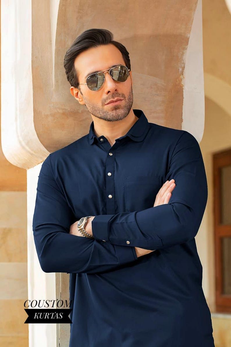 May include: A navy blue long-sleeved shirt with a button-up collar and a single button closure. The shirt has a pocket on the left chest and the text "COUSTOM KURTAS" is visible in the lower left corner.