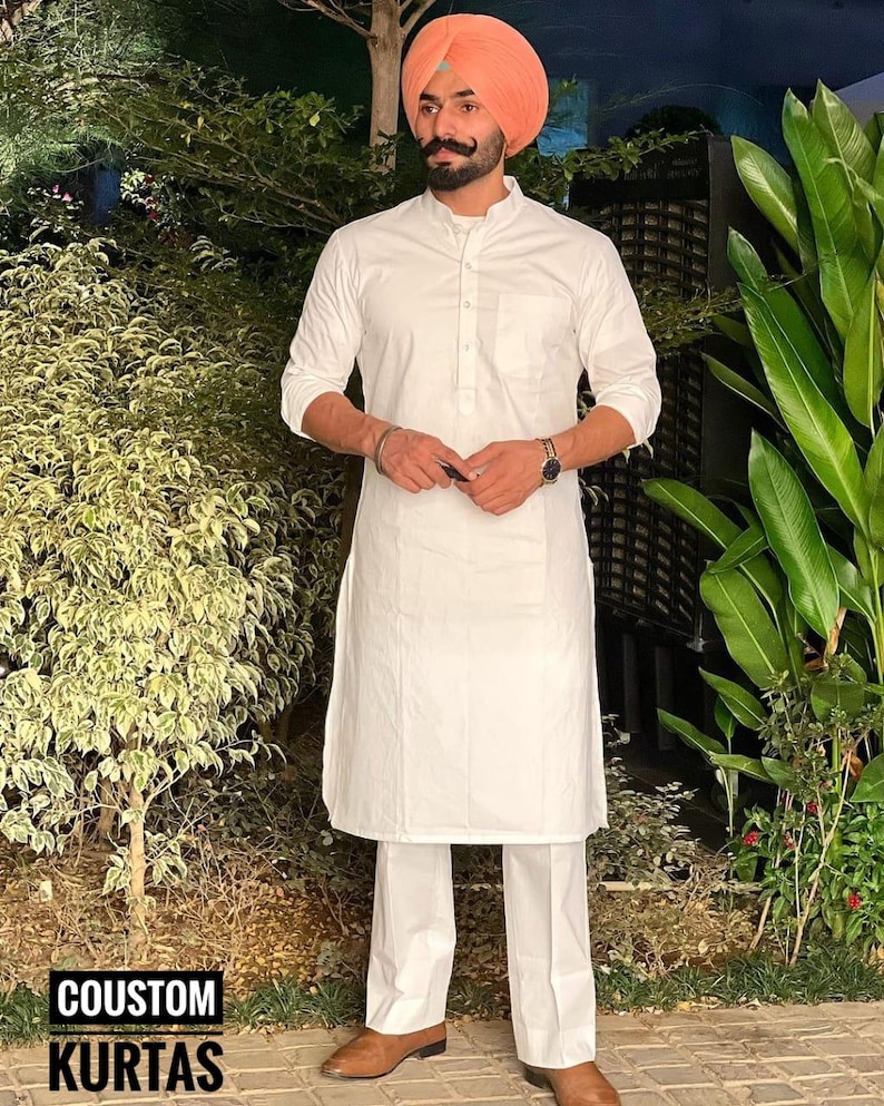 Puede incluir: Una kurta blanca de manga larga con cuello mandar&iacute;n y un solo bot&oacute;n de cierre. La kurta se combina con pantalones blancos y zapatos de cuero marr&oacute;n. La persona lleva un turbante melocot&oacute;n.