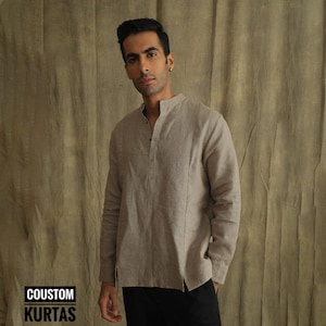 May include: A light brown linen shirt with a mandarin collar and a button-up front. The shirt has long sleeves and a relaxed fit.