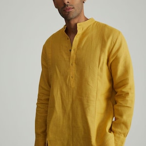 Puede incluir: Kurta de manga larga amarillo mostaza con cuello mandarín y cierre de botones. La camisa tiene costuras verticales y aberturas laterales. El texto "CUSTOM KURTAS" está en un cuadro blanco y negro en la parte inferior izquierda.