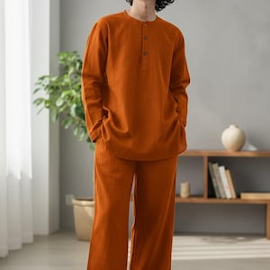 Peut inclure: Un ensemble kurta en lin orange, composé d'un haut à manches longues avec un col boutonné et d'un pantalon large assorti. L'ensemble est porté par une personne. Le texte "CUSTOM KURTAS" est en bas.