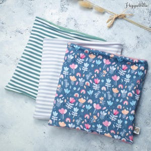 Könnte beinhalten: Drei Stoff-Halswärmer, einer mit blauem Hintergrund und einem Blumenmuster mit rosa Blüten, orangen Regenbögen und grünen Blättern, einer mit grau-weißen Streifen und einer mit grün-weißen Streifen.
