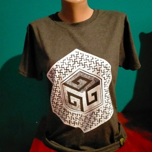 May include: A dark gray t-shirt with a white graphic of a geometric cube with a pattern inside. The cube has a stylized letter "G" on each side.
